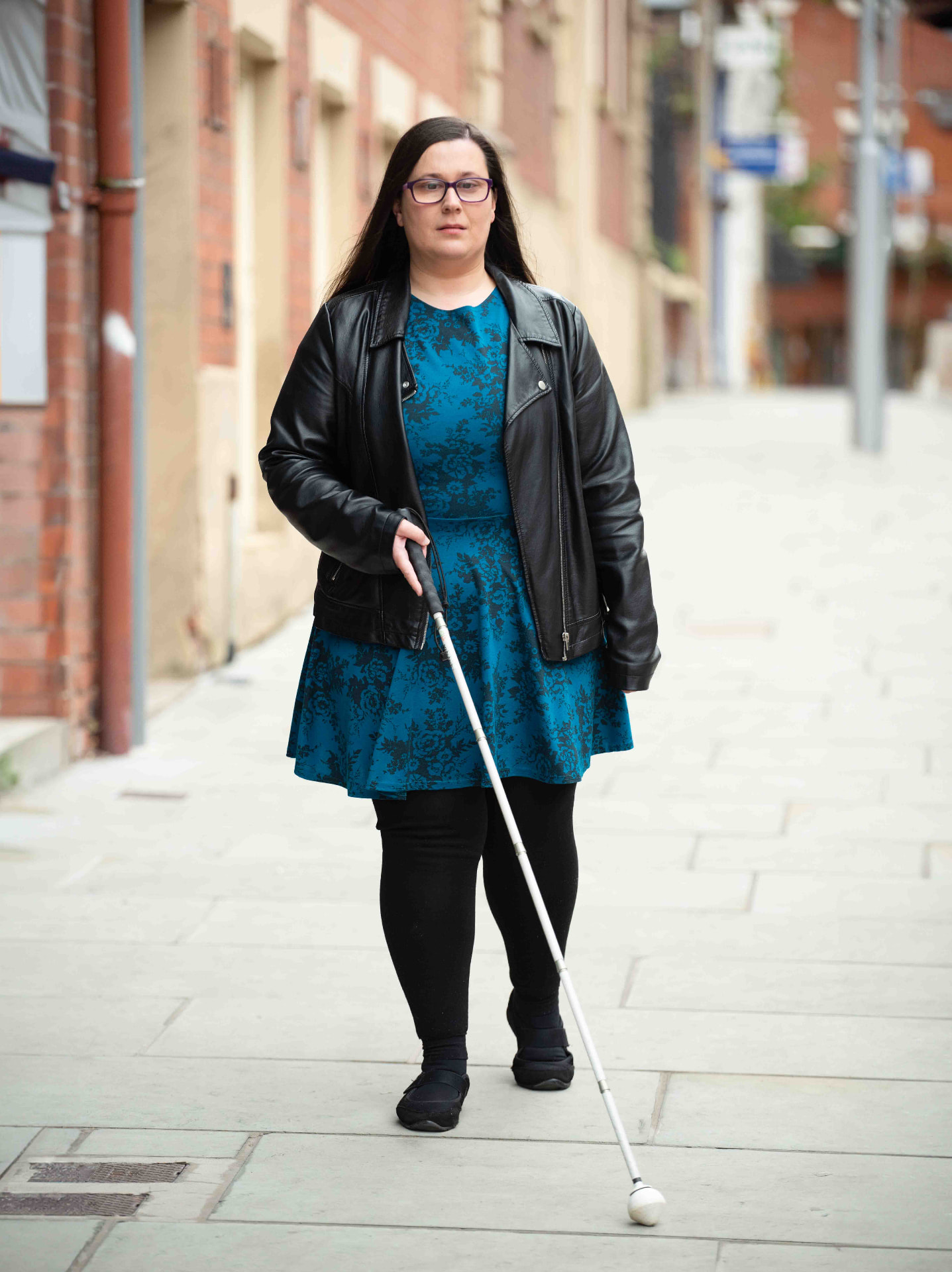 Woman with a long cane walking on a city street, photographed for a sight-loss charity campaign