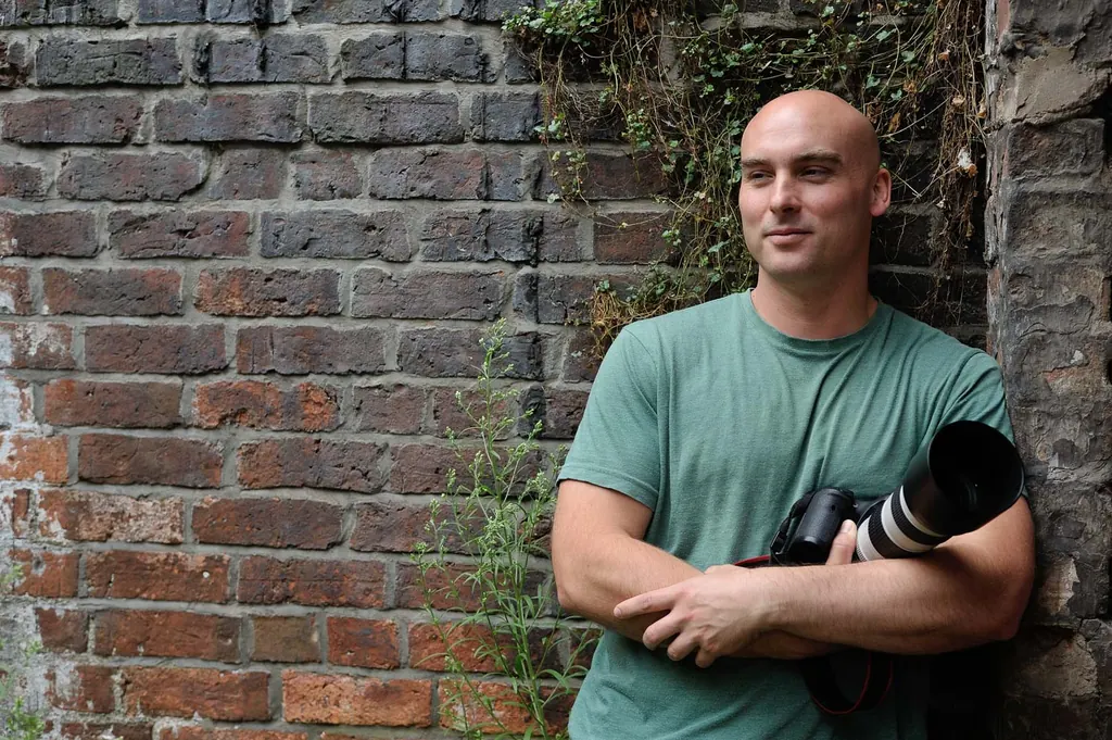 Jonathan Firin, commercial photographer, with camera against a brick wall in Bristol