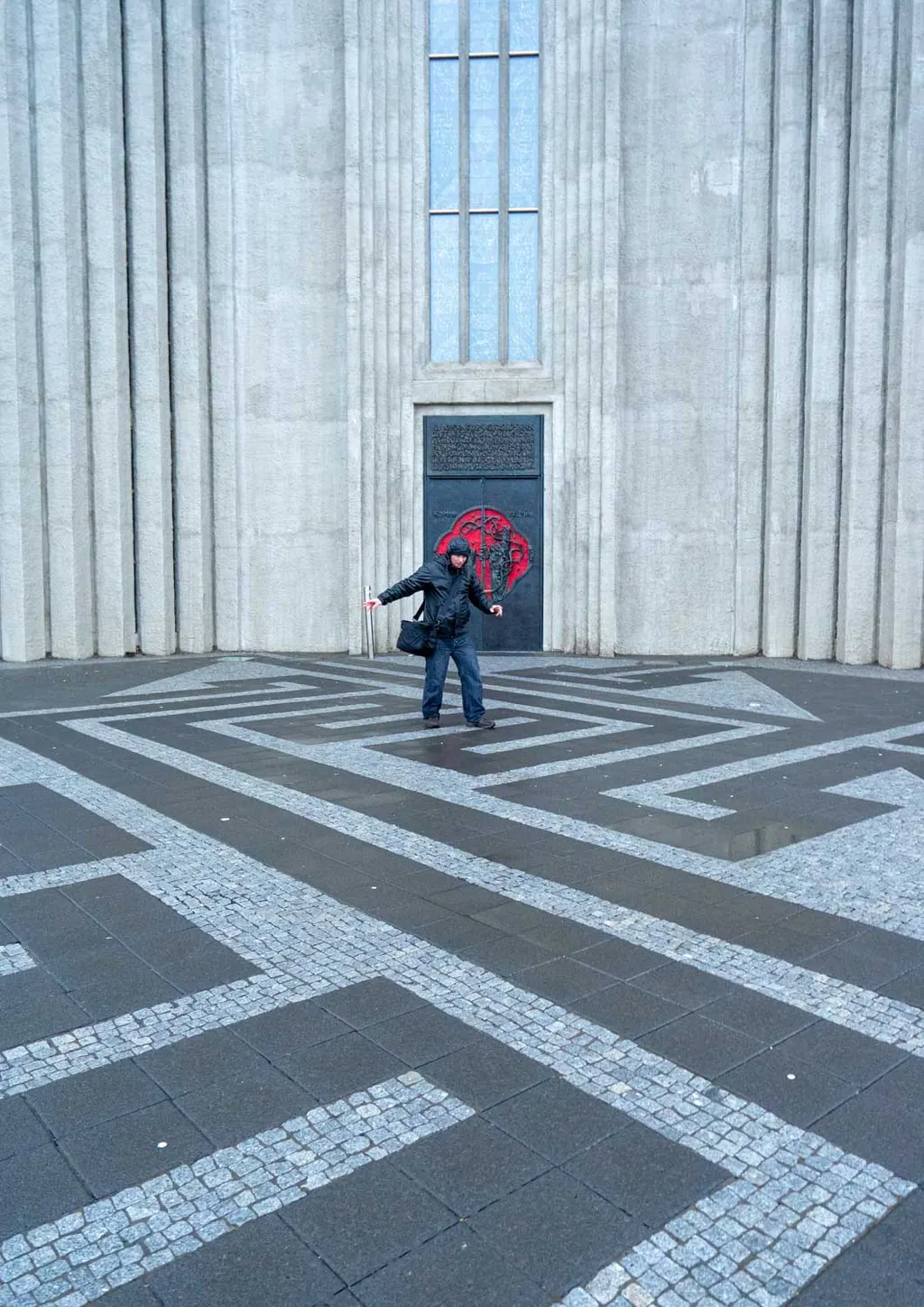 Lone figure walking across the patterned plaza in front of a concrete cathedral facade